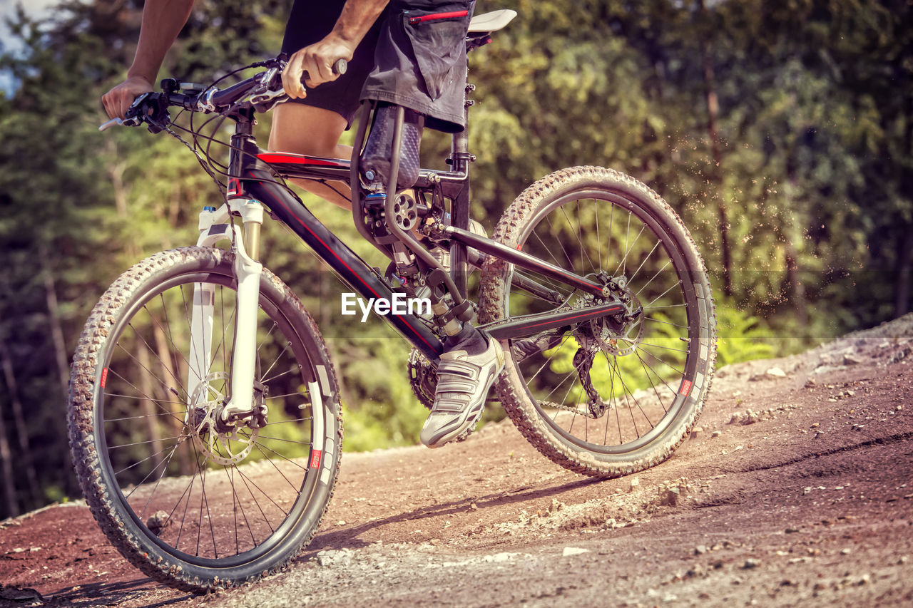 Low section of man with prosthetic leg riding bicycle on field