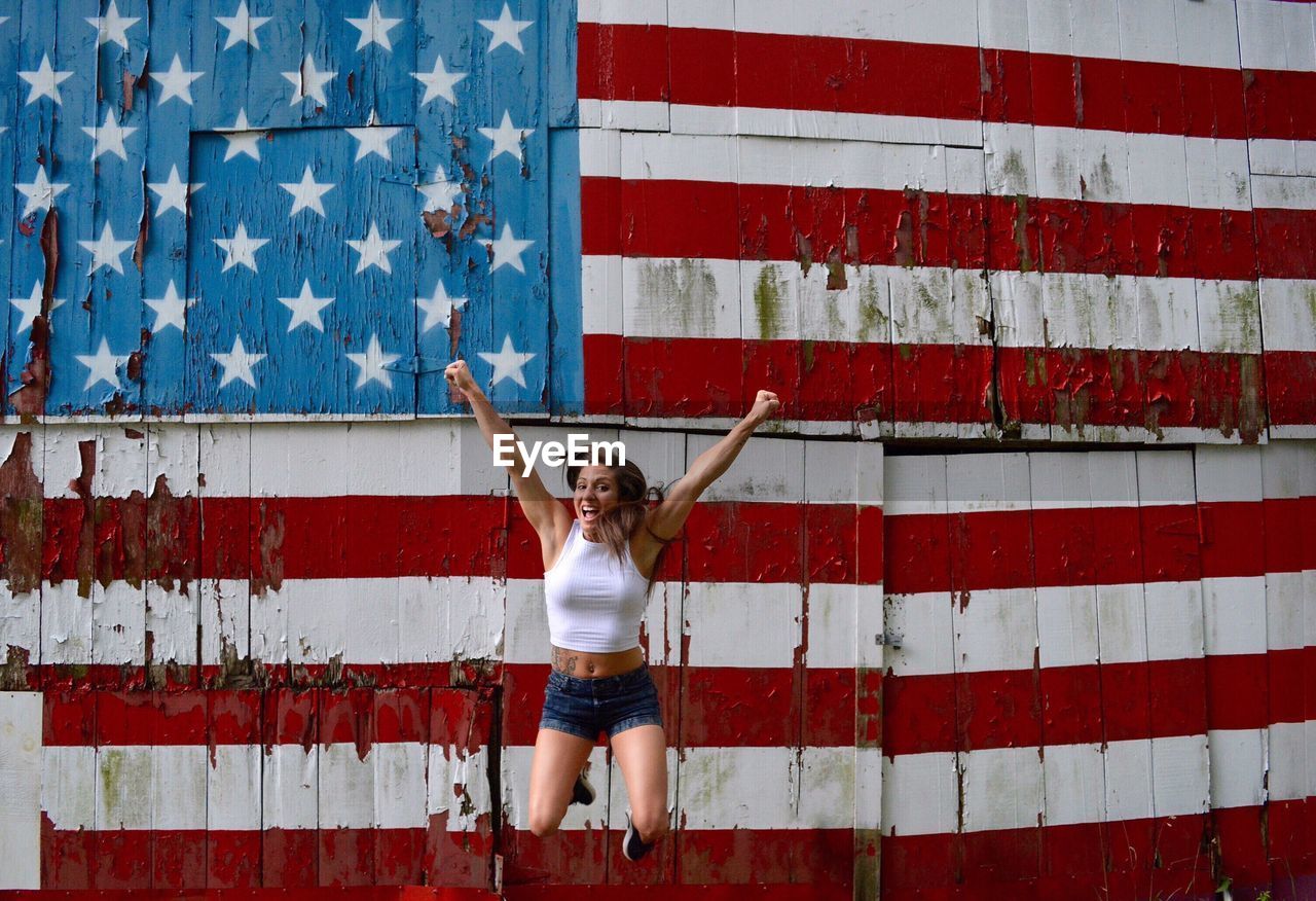 Excited woman jumping against american flag painted on wall