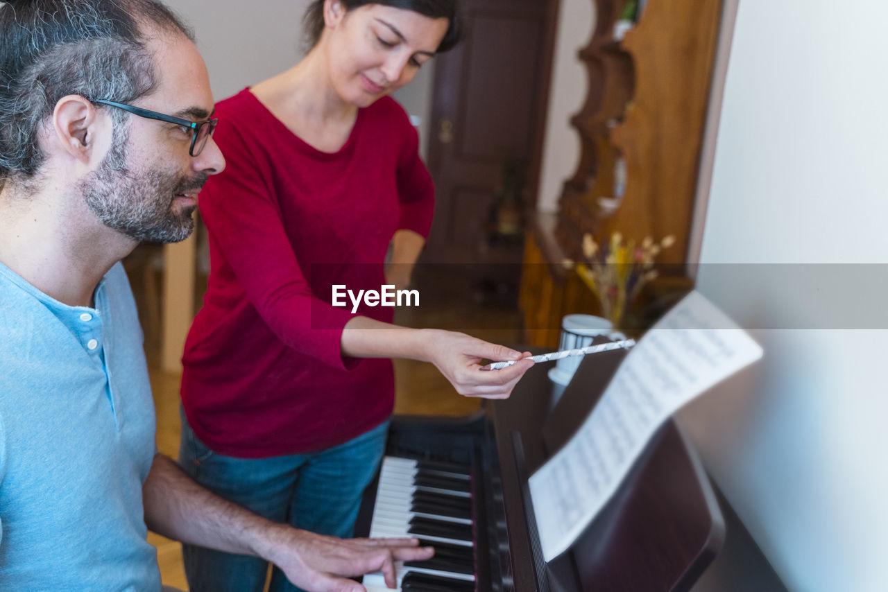 Woman teaching man to play piano at home