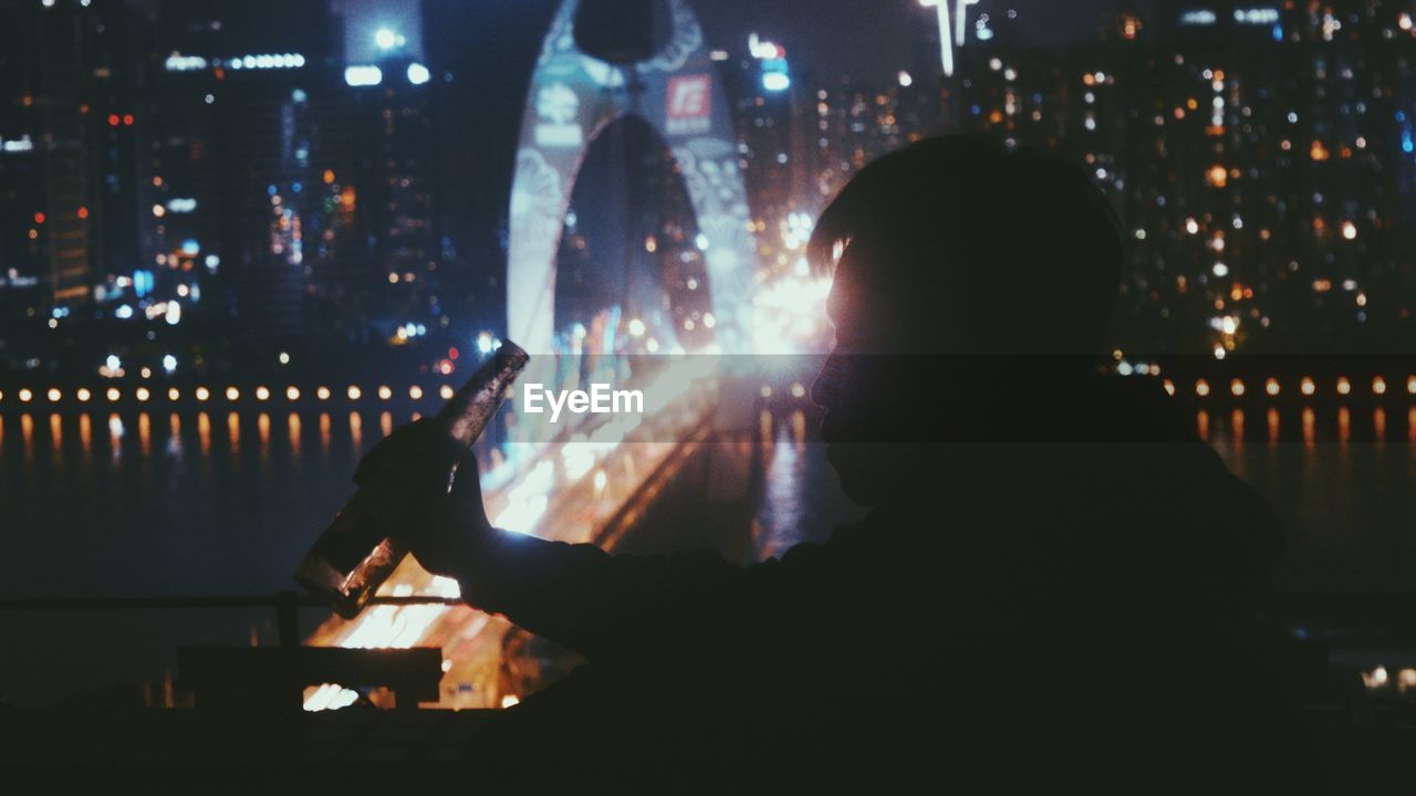 REAR VIEW OF SILHOUETTE MAN WITH ILLUMINATED CITYSCAPE AT NIGHT