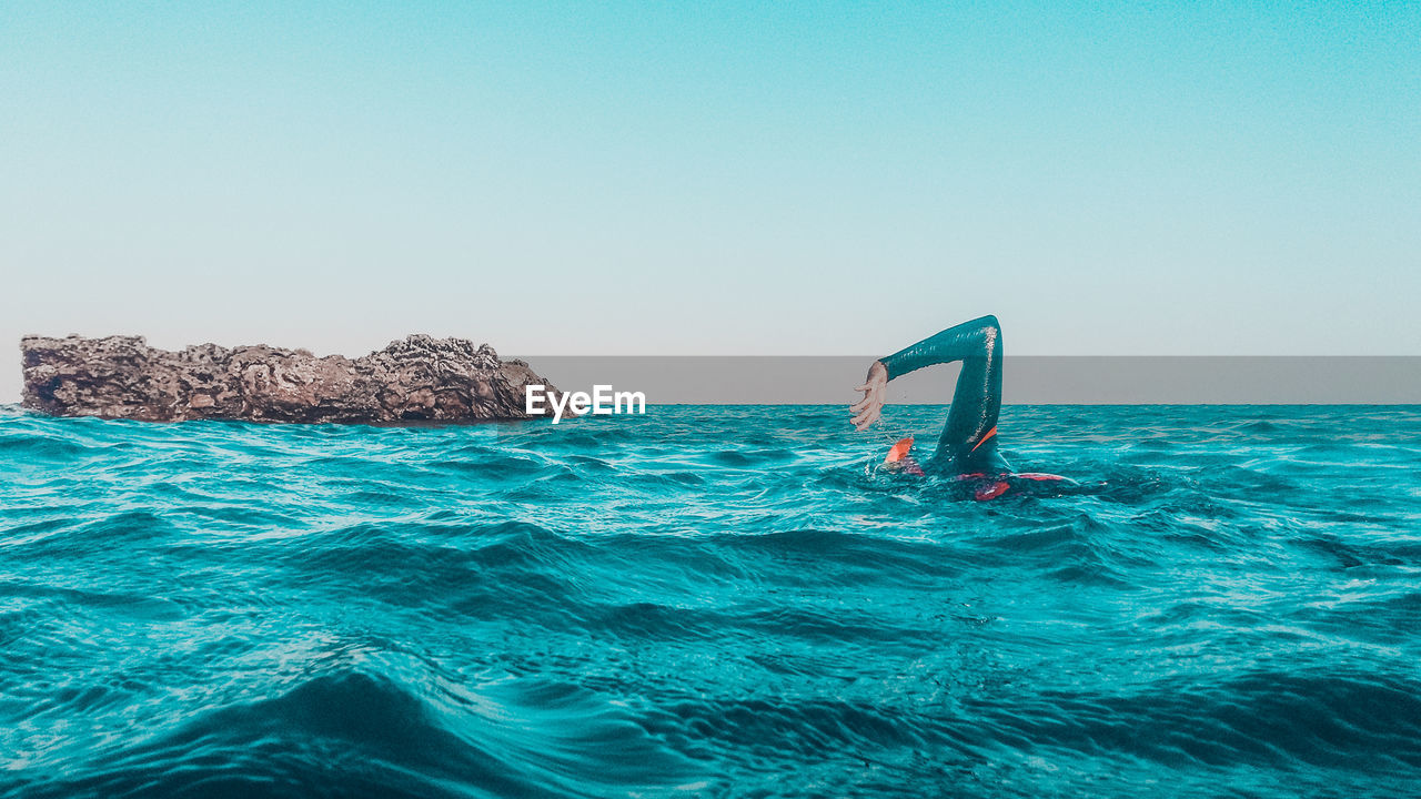 Man swimming in sea against clear sky