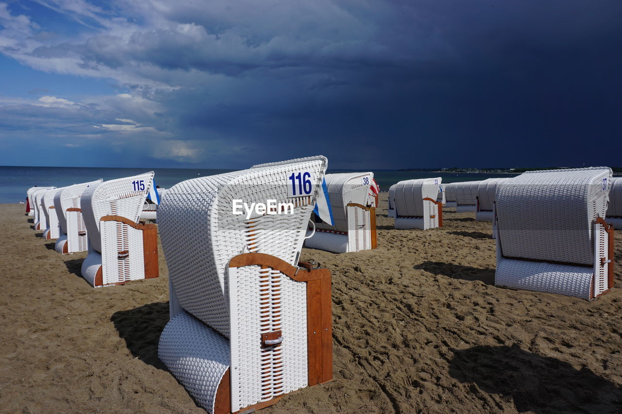 Hooded chairs on beach against sky