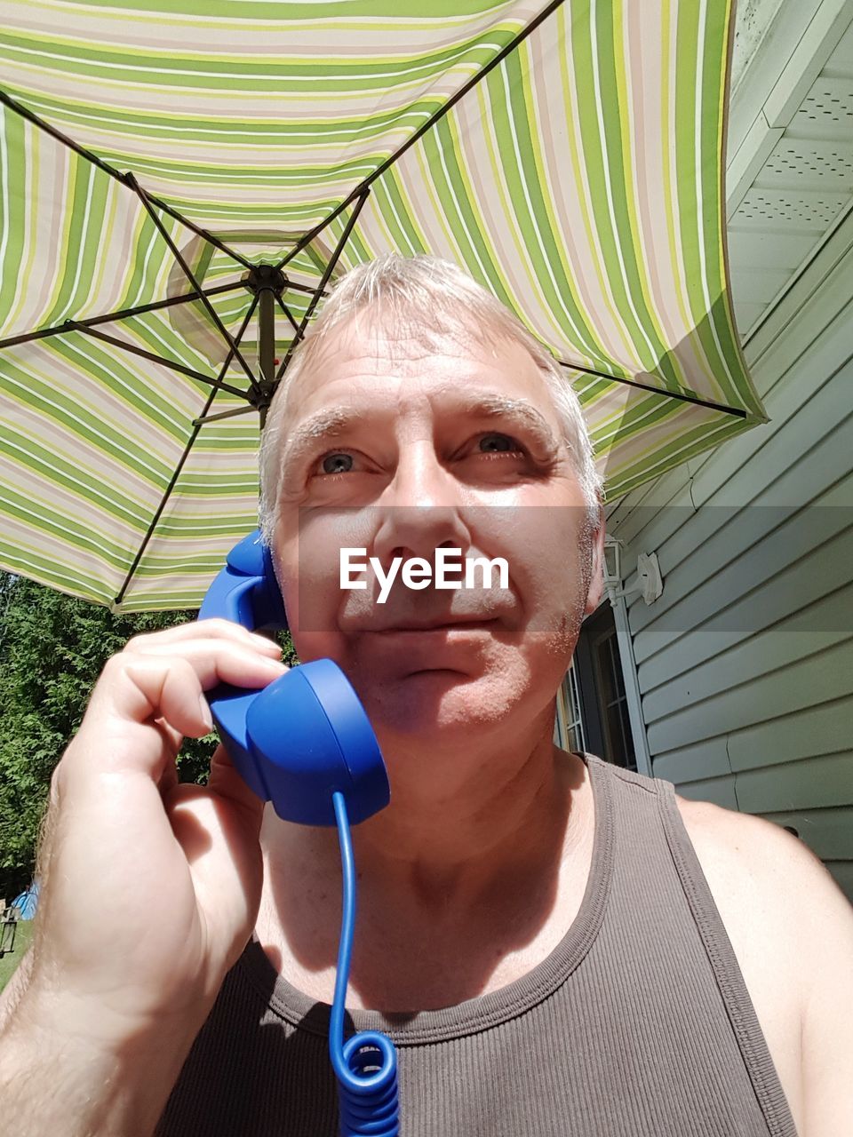 Mature man talking on landline phone while standing against parasol