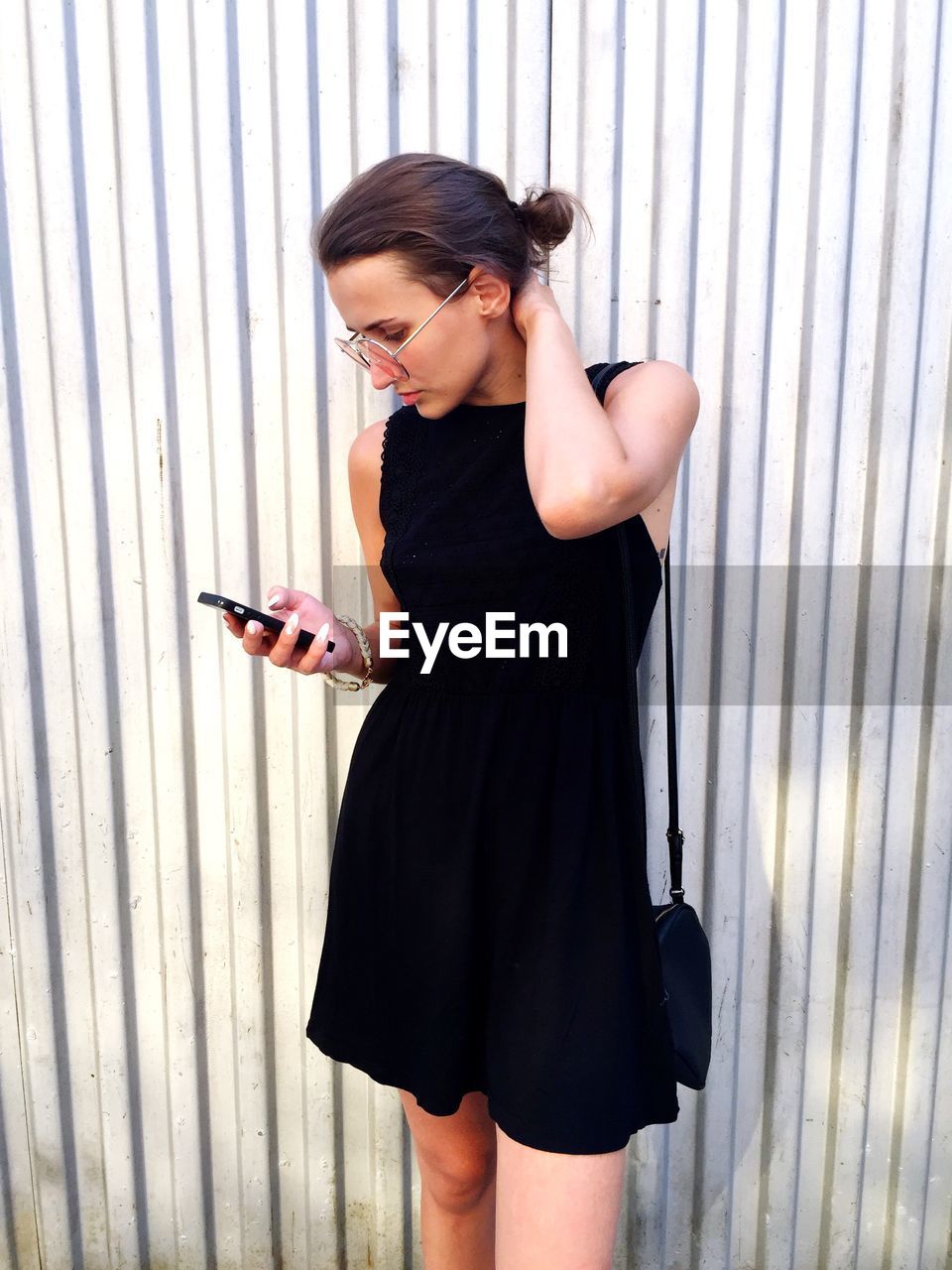 Young woman using mobile phone while standing against fence