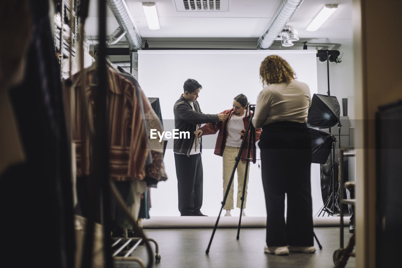 Male design professional assisting fashion model during photo shoot in studio