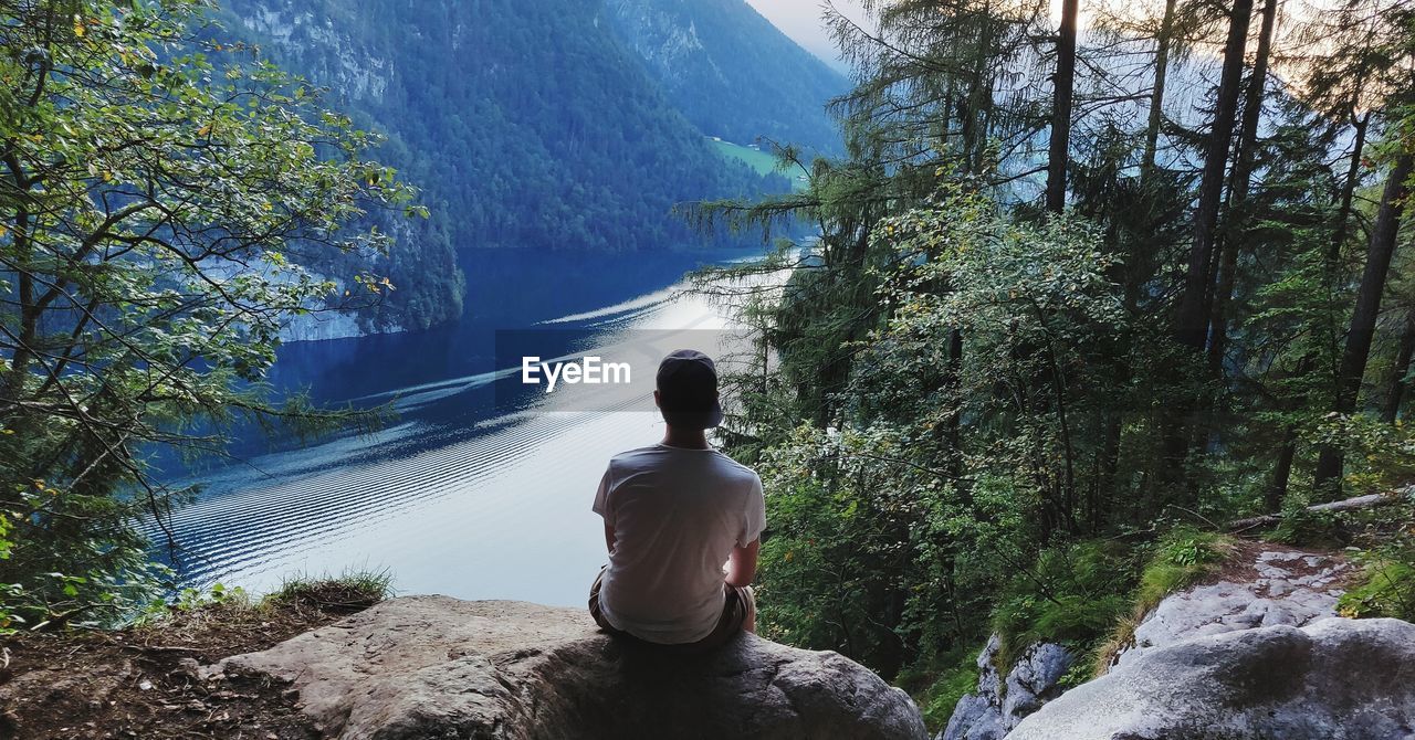 Rear view of hiker sitting on cliff against river