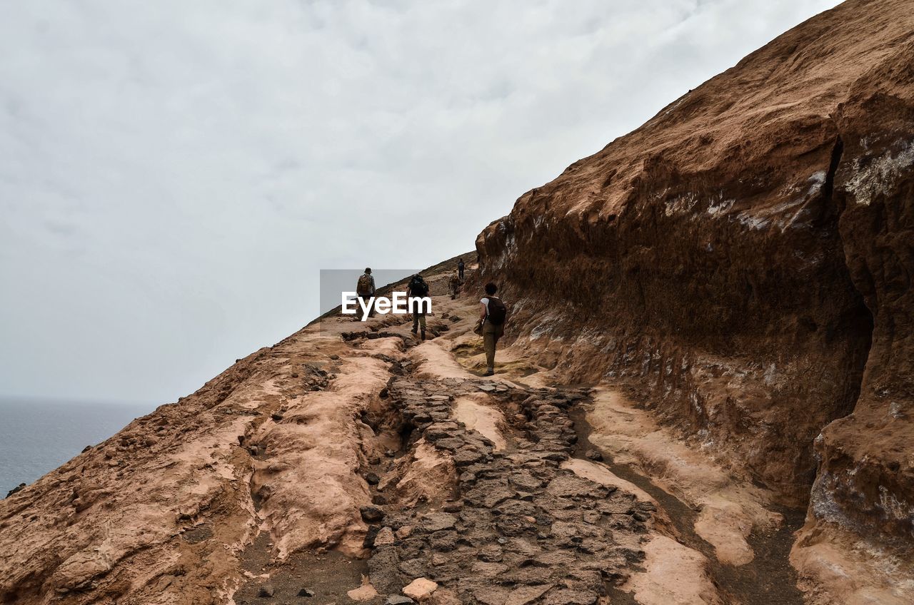 Low angle view of people on rock formation against sky