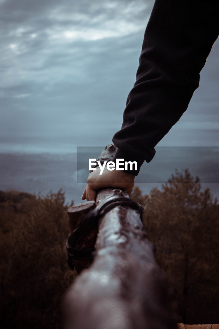 Close-up of hand holding wood against sky