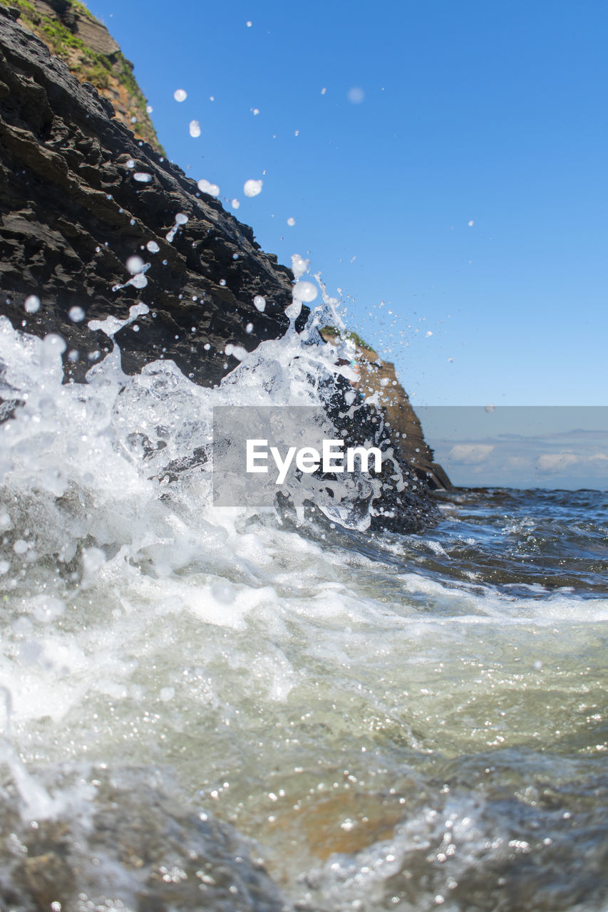 SEA WAVES SPLASHING ON SHORE AGAINST CLEAR SKY