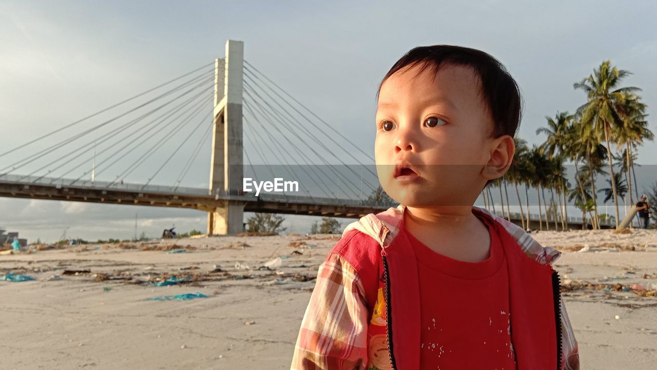 Portrait of boy standing on bridge against sky