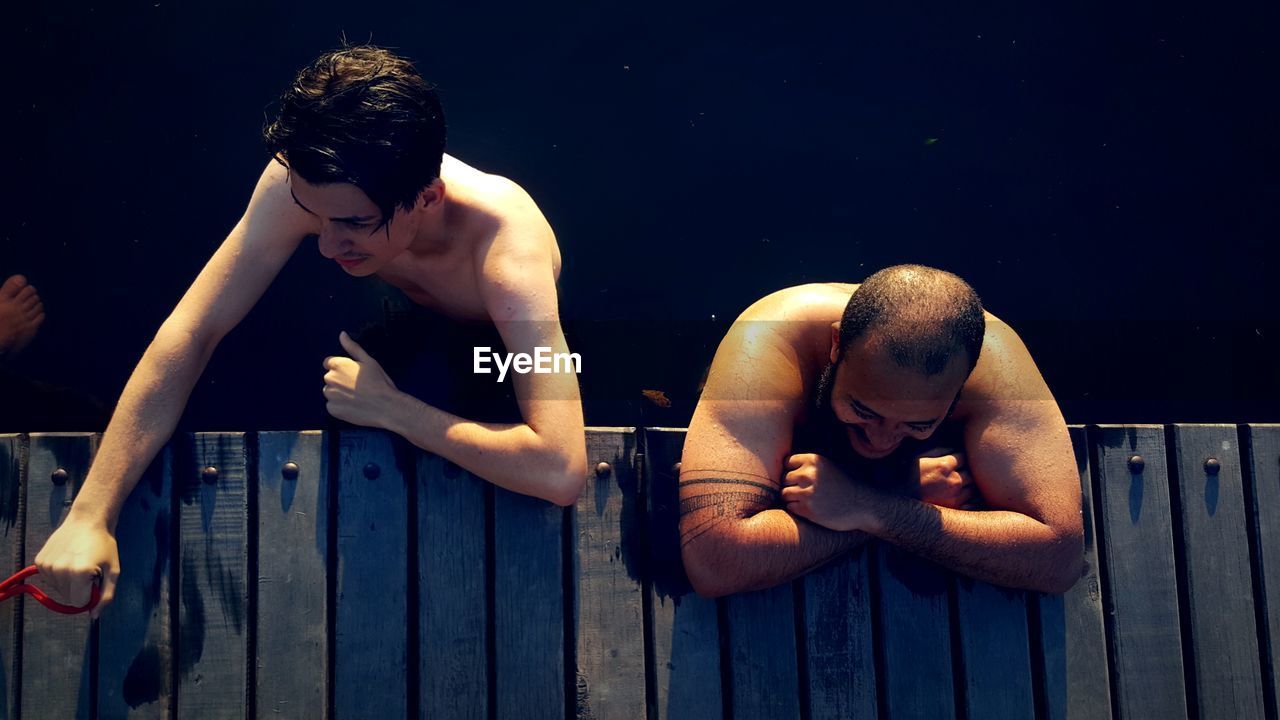 High angle view of shirtless male friends standing at jetty in lake