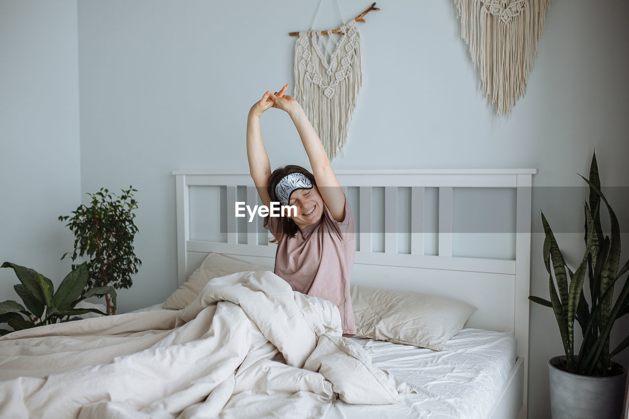 Happy young girl stretching in bed in the morning