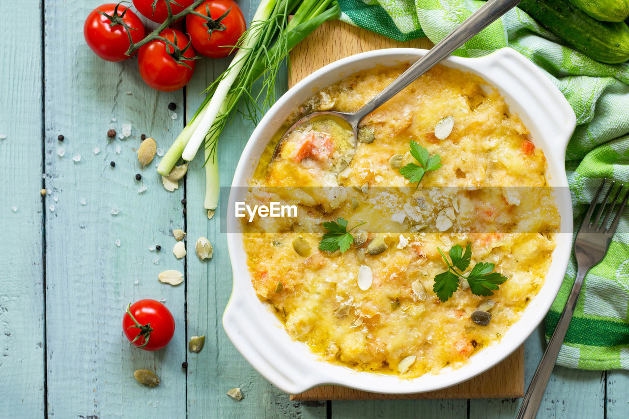 Casserole crumble with red fish, white bread and cheese on the kitchen wooden table.