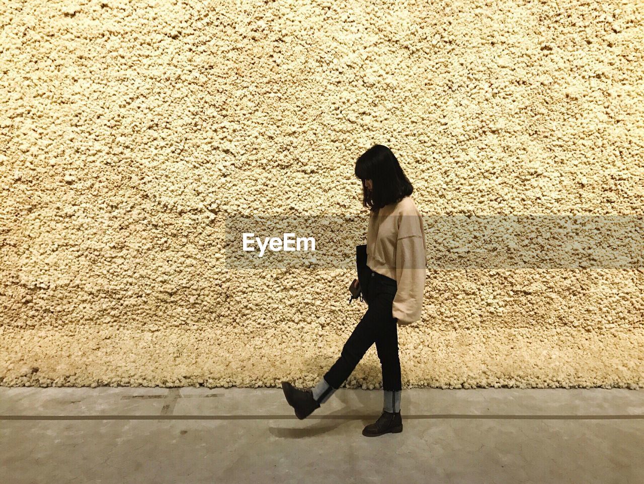 Side view of woman walking on footpath by beige wall