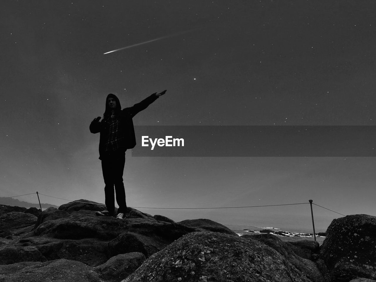 Full length of man gesturing while standing on rock against sky