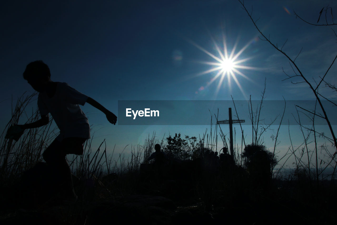 SIDE VIEW OF SILHOUETTE MAN STANDING ON FIELD AGAINST BRIGHT SUN