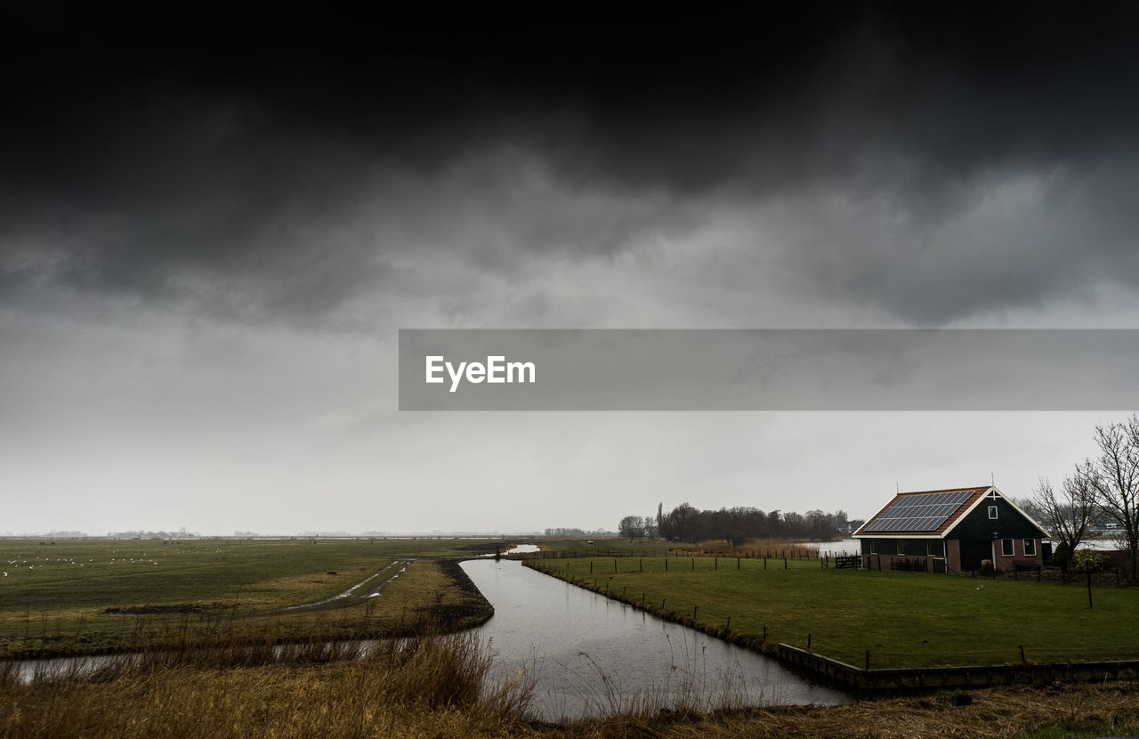 Scenic view of field by houses against sky