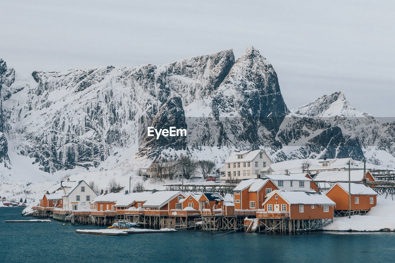 Buildings by snowcapped mountains against sky