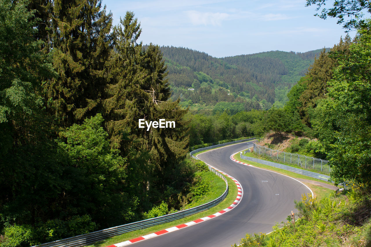 Road amidst trees and mountains against sky