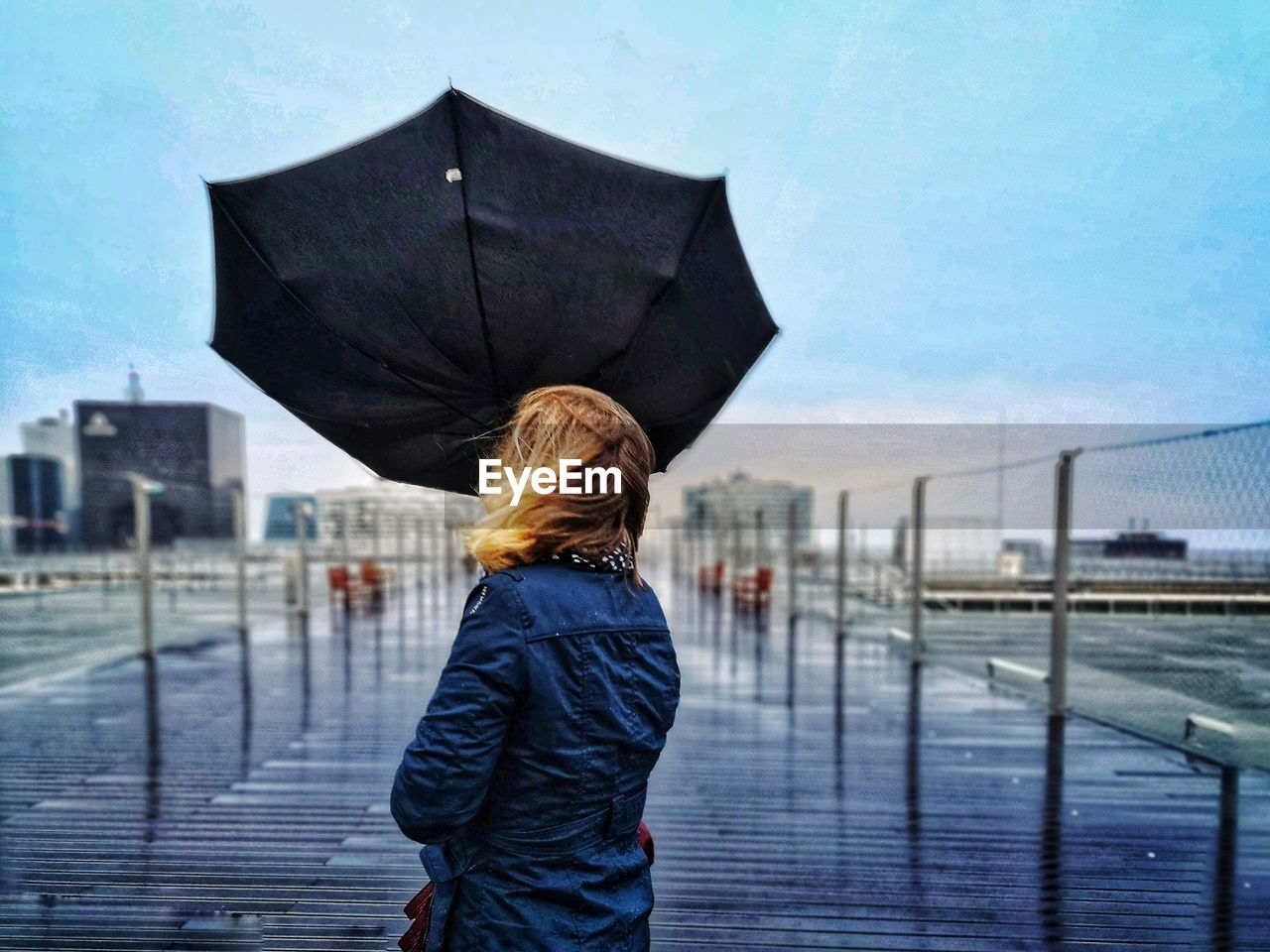 Rear view of woman holding umbrella while standing by railing against sky