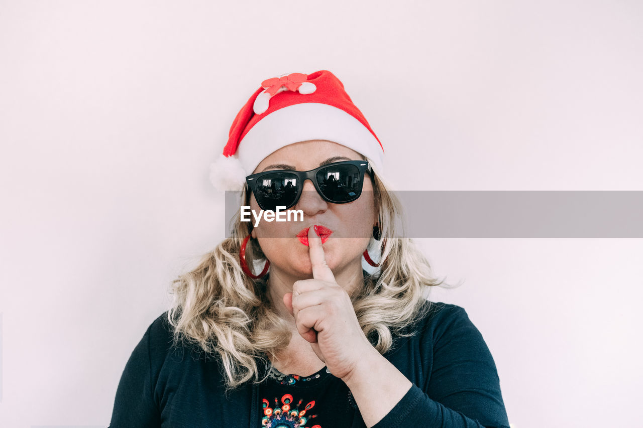 Portrait of woman wearing sunglasses while gesturing against wall