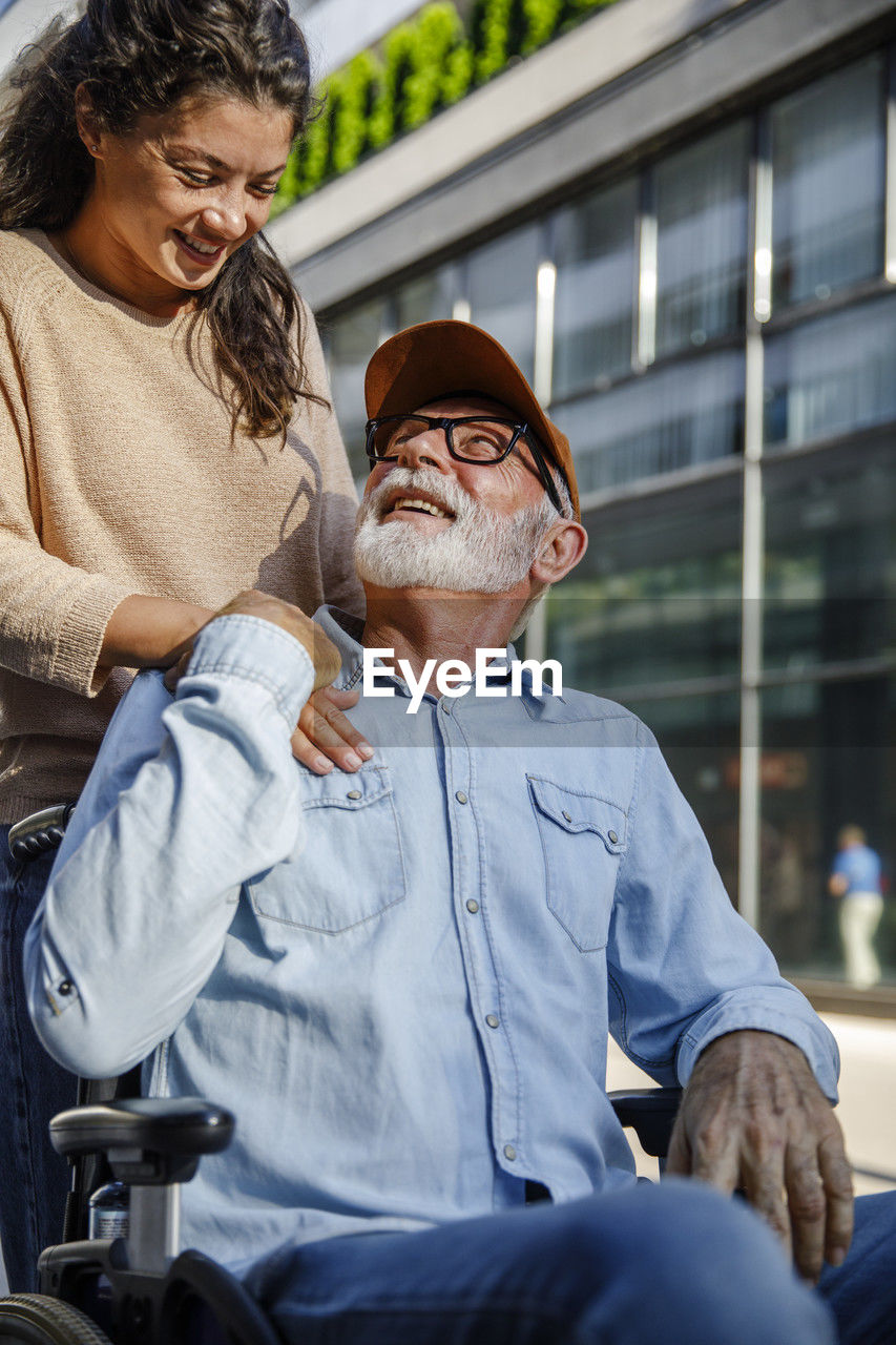 Smiling caregiver with hand on shoulder looking at senior man in wheelchair