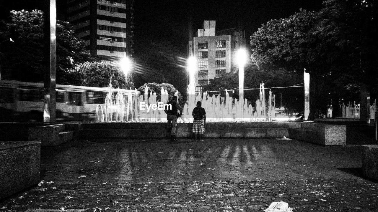 WOMAN STANDING ON ILLUMINATED STREET AT NIGHT