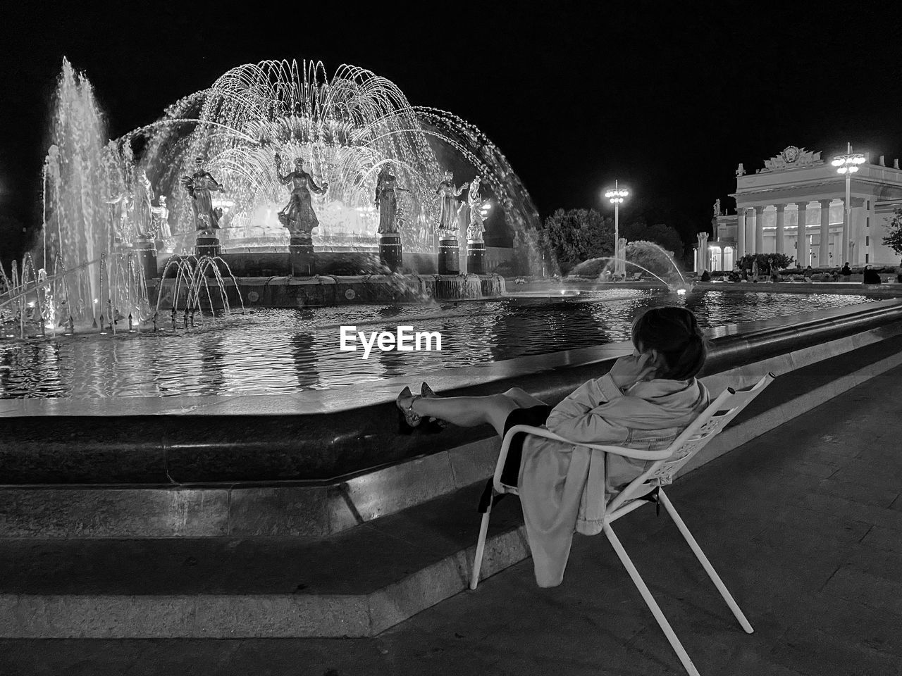Rear view of girl sitting on illuminated water at night