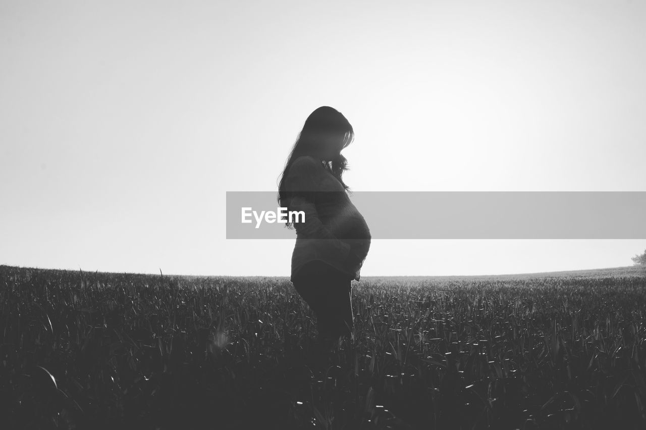 Pregnant woman standing on field against sky during sunny day