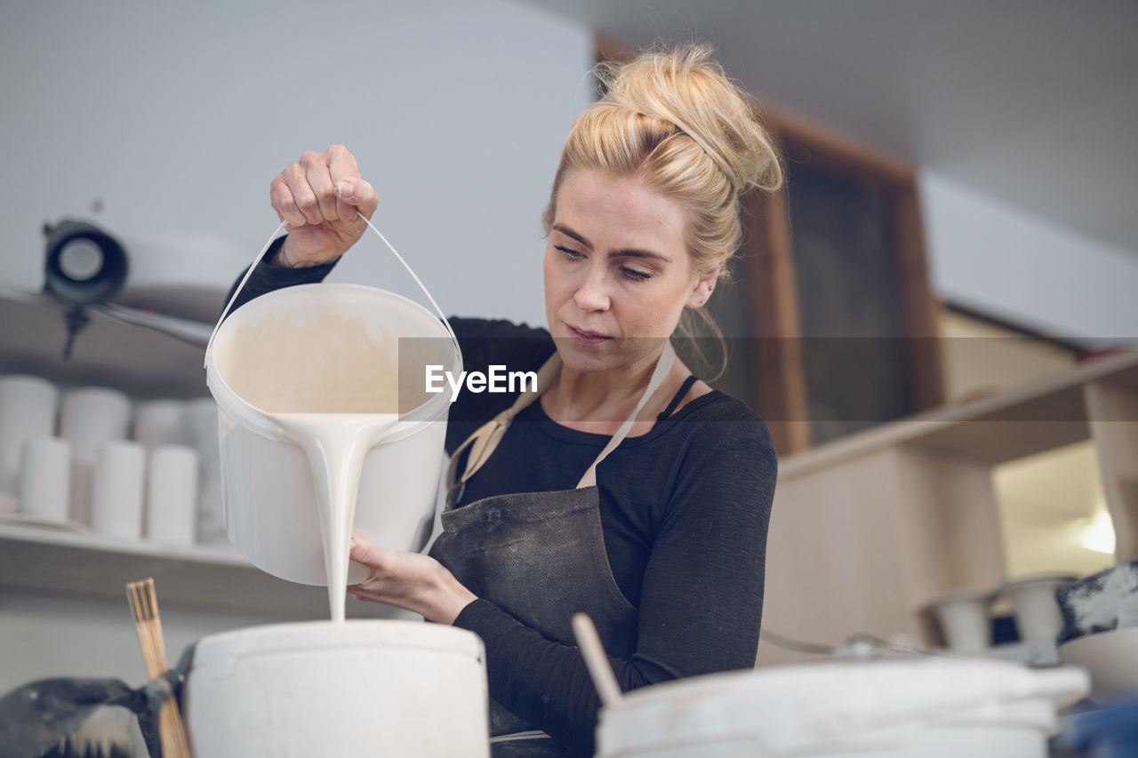 Low angle view of woman pouring paint in container at workshop