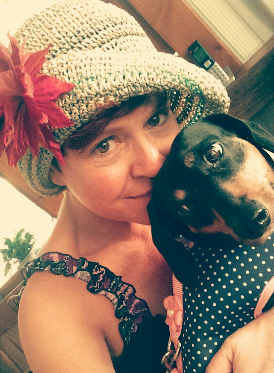 Portrait of woman wearing hat embracing dog at home