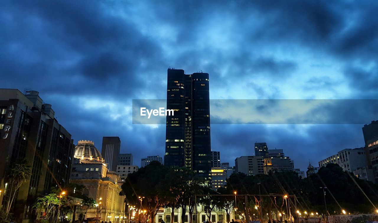 VIEW OF ILLUMINATED CITYSCAPE AGAINST CLOUDY SKY