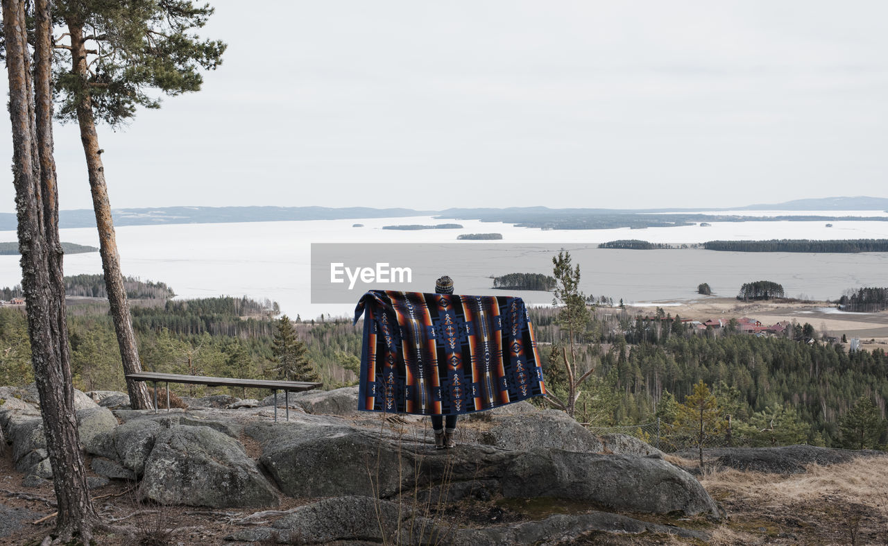 Woman holding blanket standing on a rock with a beautiful view