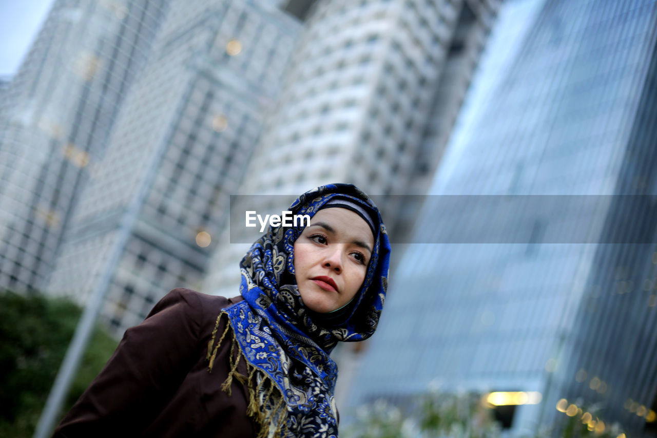 PORTRAIT OF YOUNG WOMAN AGAINST MODERN CITY