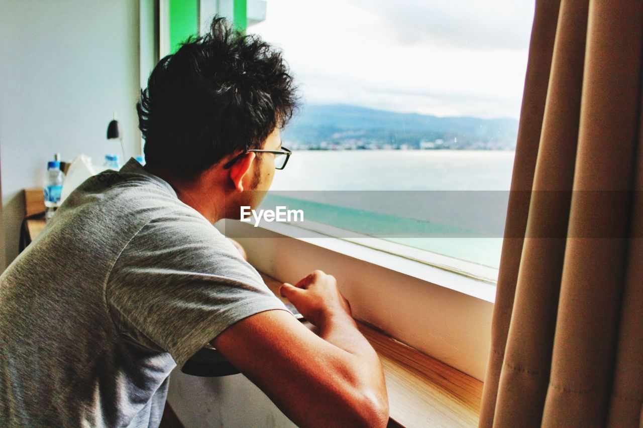 MAN LOOKING AT SEA FROM WINDOW