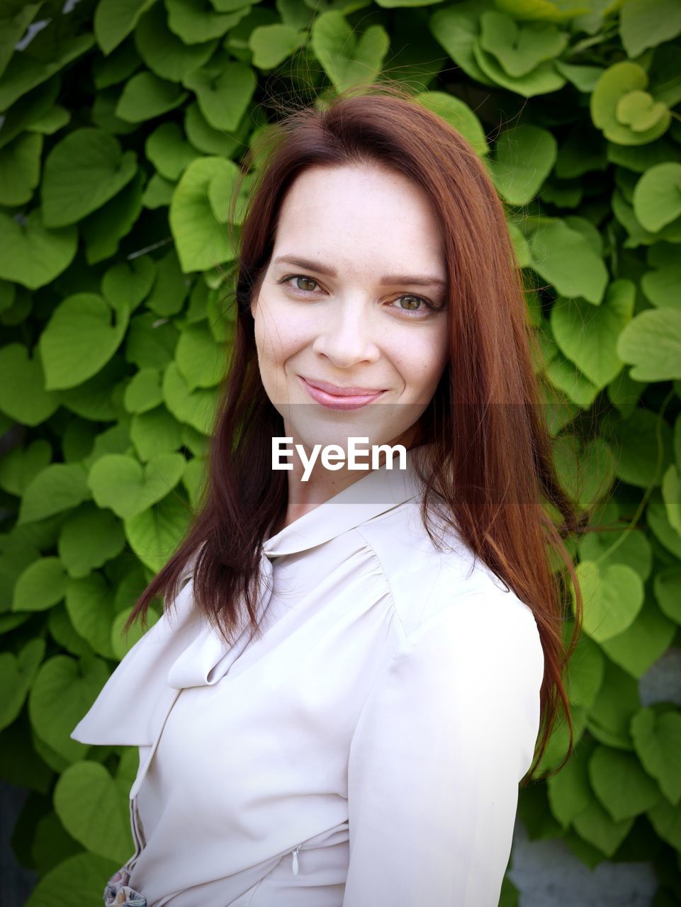 Portrait of beautiful young woman smiling while standing against ivy