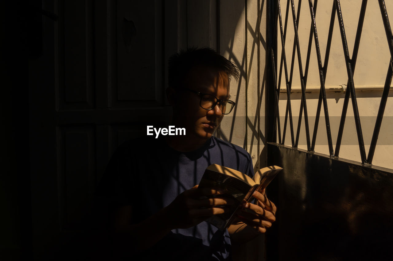 Young man reading book while sitting by gate