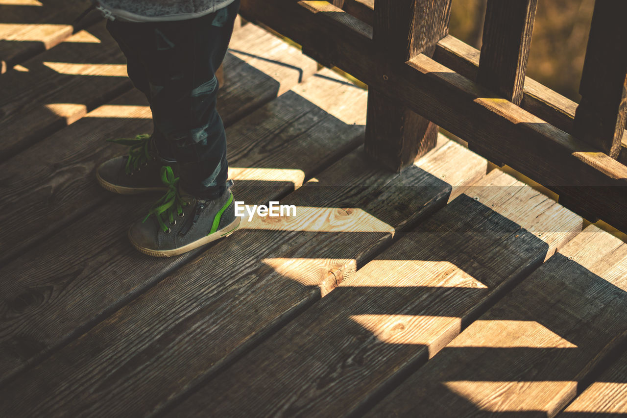 Low section of person standing on wooden boardwalk