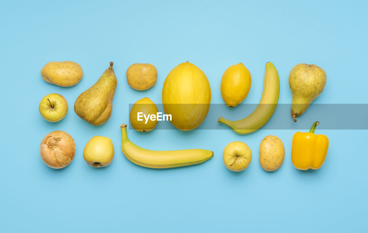 Flat lay, yellow fruits and vegetables on a blue table. vegetables and fruits arranged symmetrically