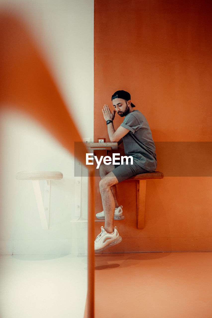 Side view of young man looking away against wall