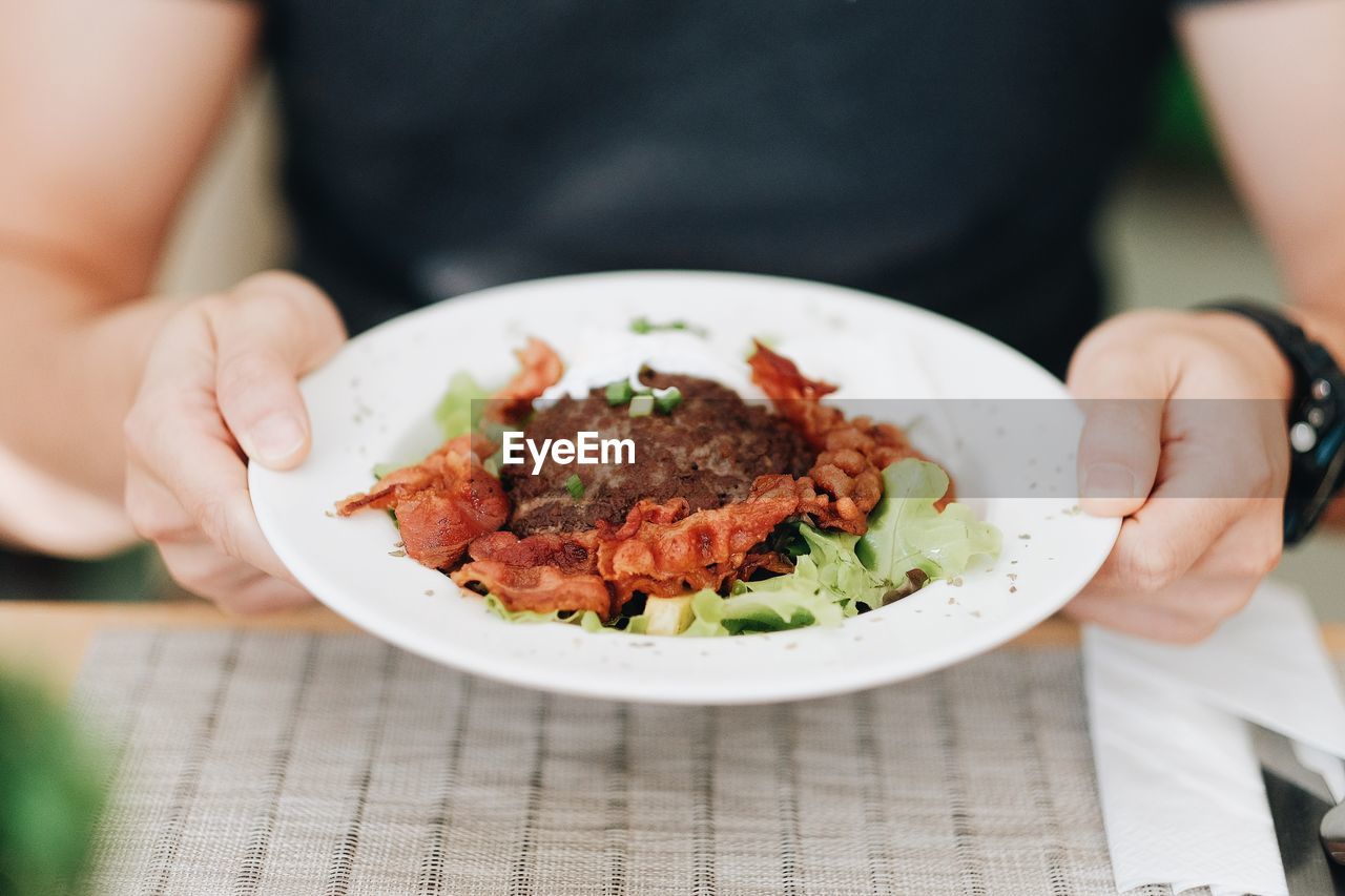 Midsection of woman holding meal in bowl at outdoor table