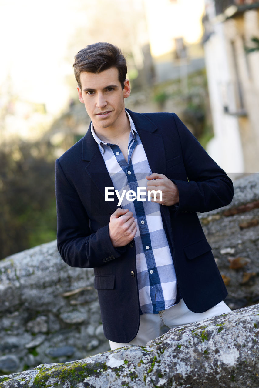Portrait of young man wearing blazer amidst retaining walls during sunset