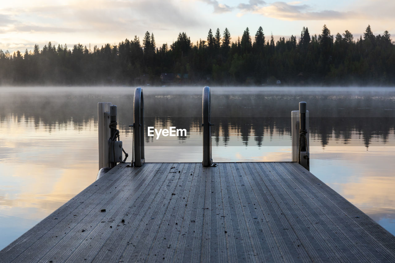 Swimming dock with ladder near calm lake at sunset with reflection