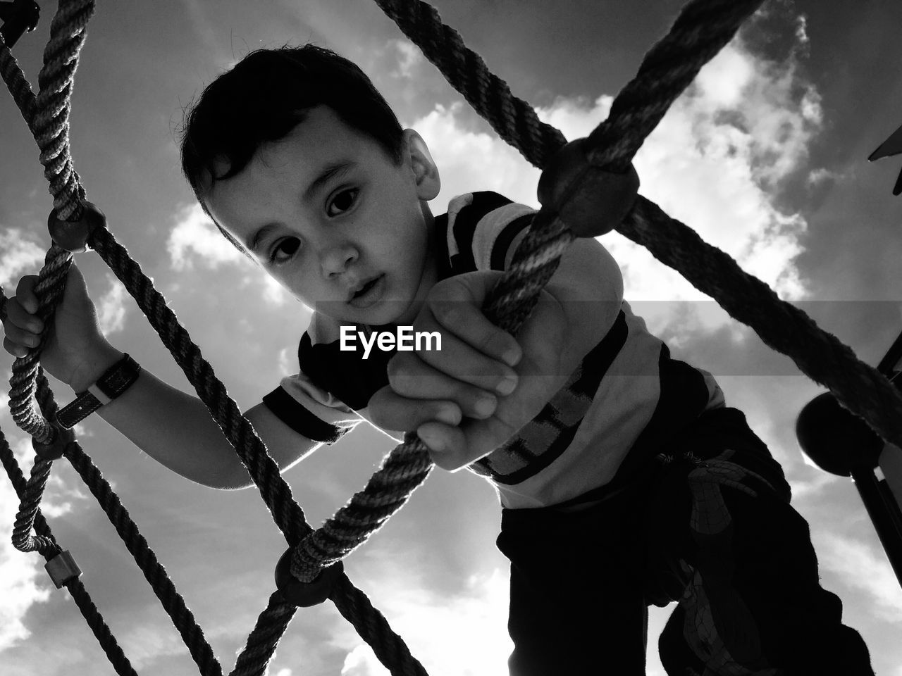 Low angle view of boy playing on jungle gym against sky
