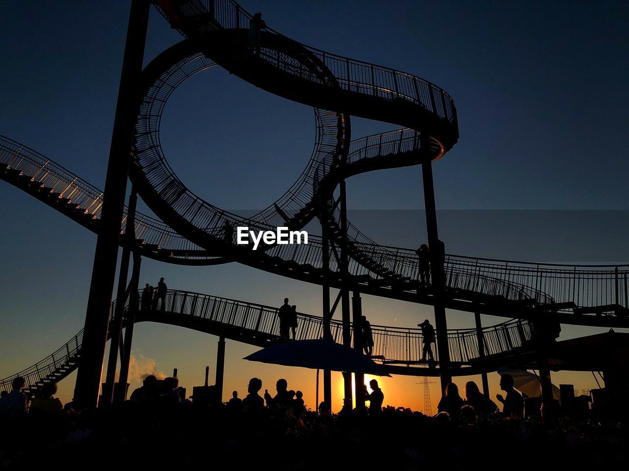 Silhouette people at amusement park against sky during sunset