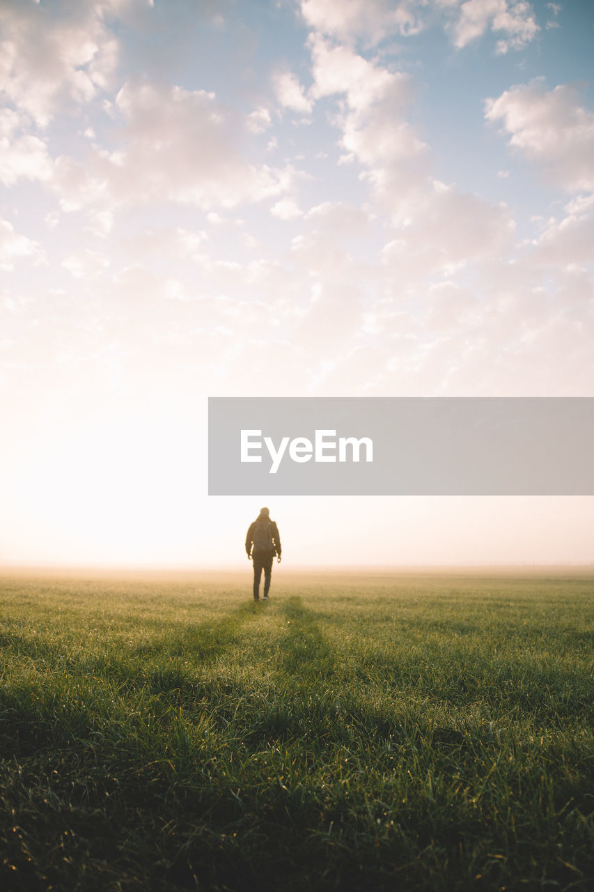 Man walking on field against sky during sunset