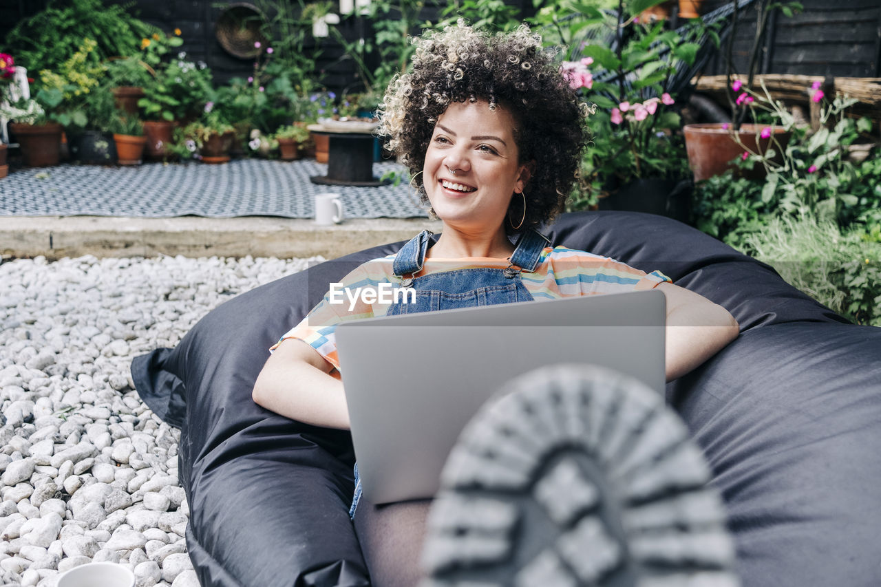 Smiling woman with laptop relaxing on bean bag