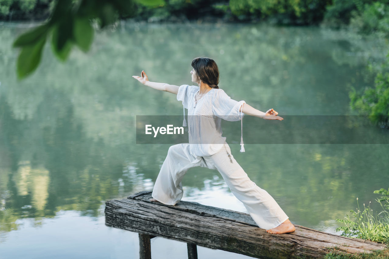 Yoga by the lake - young woman practicing warrior 2 pose or virabhadrasana ii