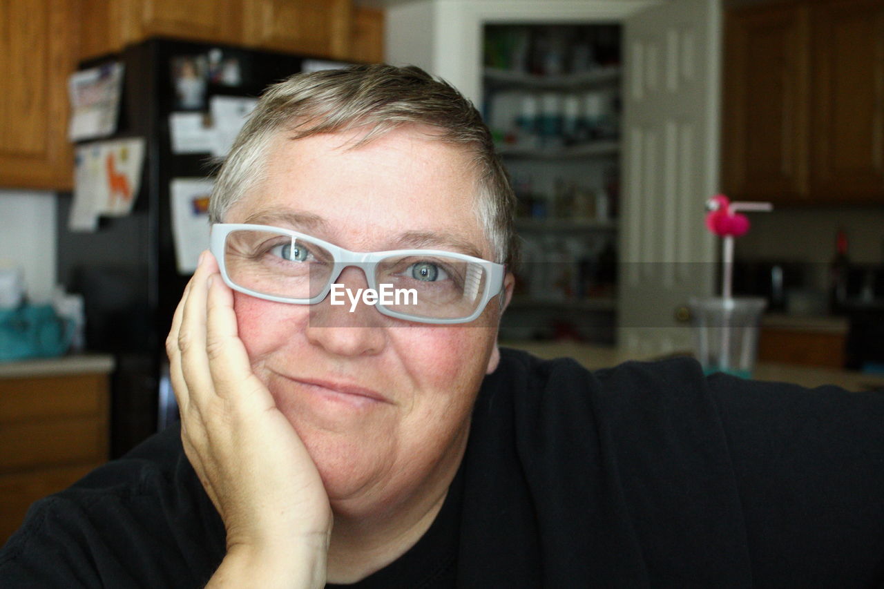 Close-up portrait of mature woman smiling with hand on chin at home