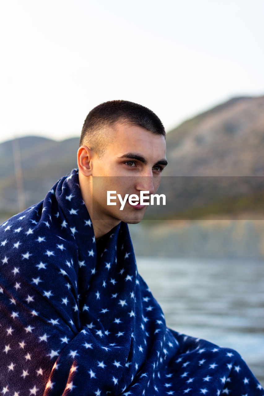 Portrait of a beautiful young man in a blue plaid, in summer on the background of the sea coast
